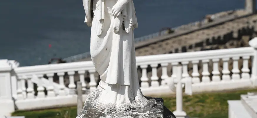 Escultura religiosa de piedra en el cementerio de Luarca con el mar de fondo.