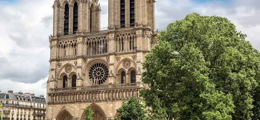 Fachada principal de la Catedral de Notre Dame en París, con dos torres góticas, gran rosetón central y tres portales ornamentados, bajo un cielo despejado.