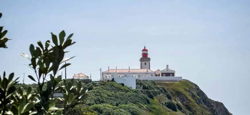 Faro de Cabo da Roca sobre un acantilado rodeado de vegetación y cielo claro.