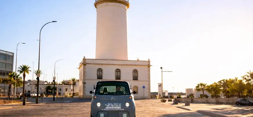 Coche eléctrico de tour frente al faro La Farola en el puerto de Málaga.