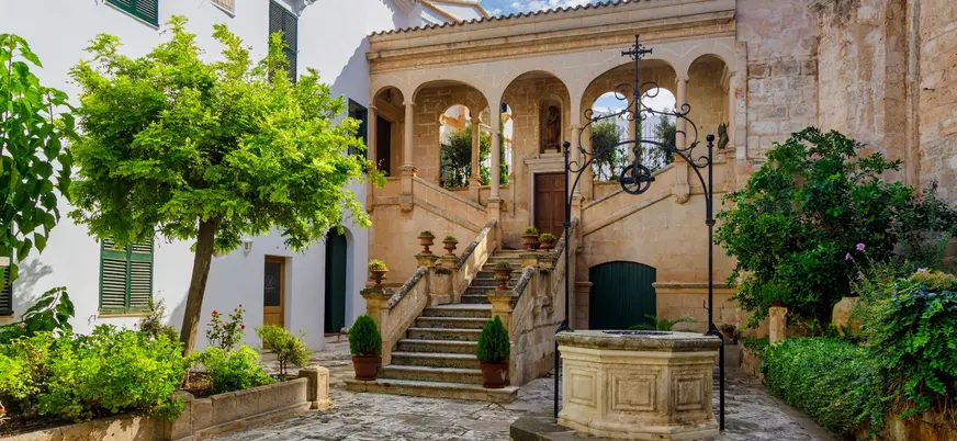 Patio de piedra con pozo antiguo, escalera y arcos en Ciutadella de Menorca