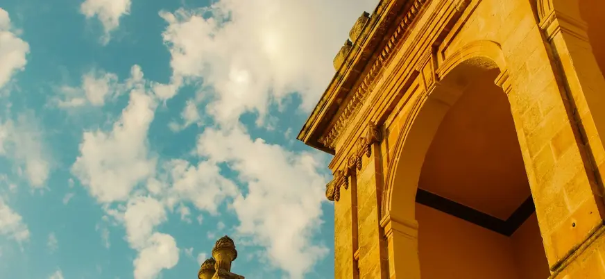 Arquería de piedra dorada en Ciutadella bajo un cielo azul con nubes dispersas