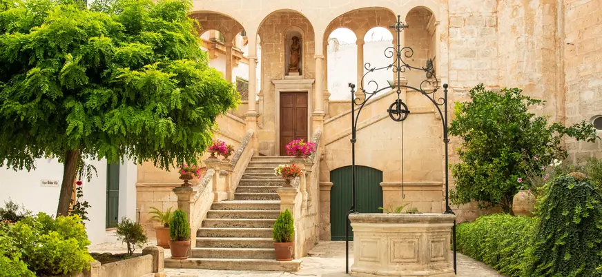 Patio mediterráneo con pozo de piedra, flores y arquería en Ciutadella de Menorca
