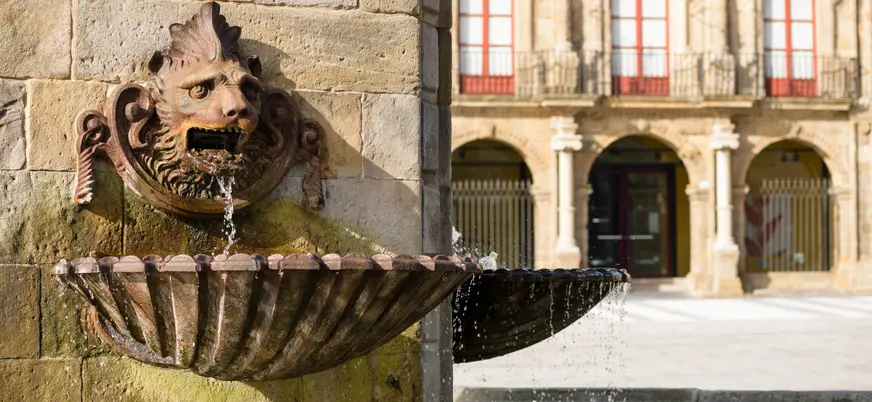 Fuente del Monumento a Pelayo con detalle escultórico en piedra y fachada del Palacio de Revillagigedo en Gijón.