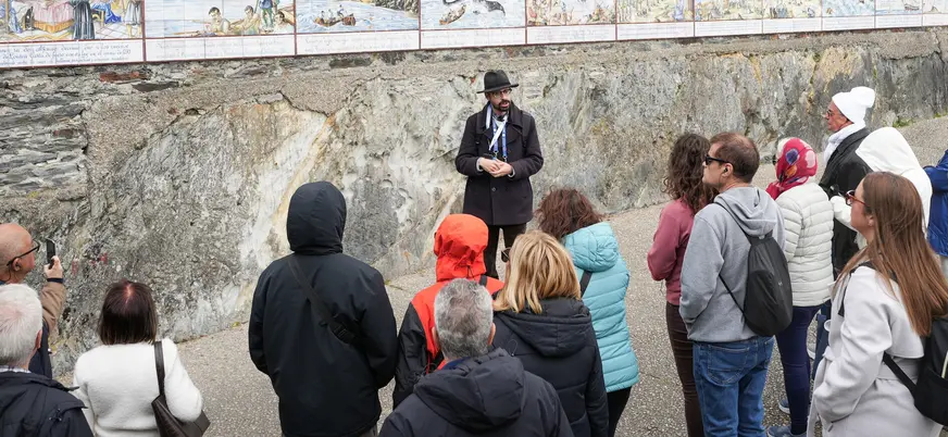 Guía explicando la historia de Luarca ante un mural de azulejos en Asturias