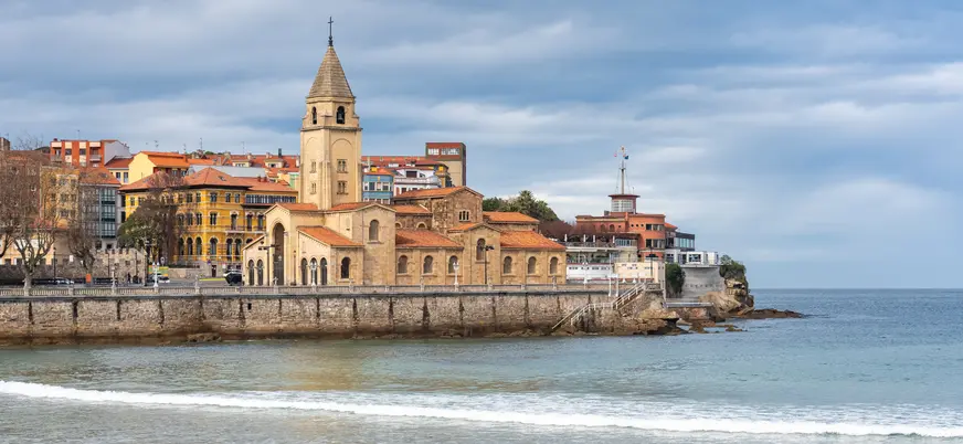 Iglesia de San Pedro Apóstol junto al mar en Gijón, con el casco antiguo y la playa de San Lorenzo al fondo
