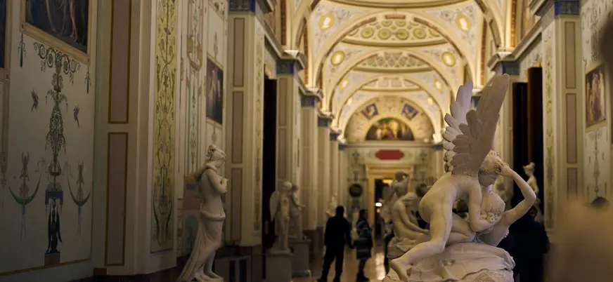 Interior de la Galería Uffizi en Florencia, con un pasillo ornamentado y esculturas clásicas de mármol, destacando en primer plano la obra 'Psique reanimada por el beso de Cupido.