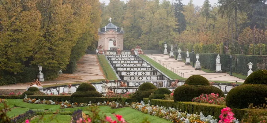 La Cascada Nueva de La Granja rodeada de árboles otoñales y estatuas blancas.