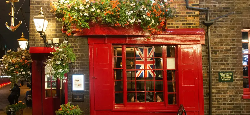 Fachada de un pub tradicional con flores y la bandera británica en Londres.