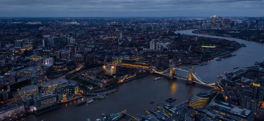 Vista aérea panorámica del río Támesis en Londres con el Puente de la Torre iluminado y la Torre de Londres al anochecer.