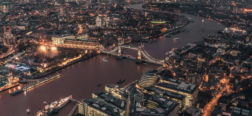 Vista aérea nocturna de Londres con el Tower Bridge iluminado cruzando el Támesis y la Torre de Londres en primer plano.