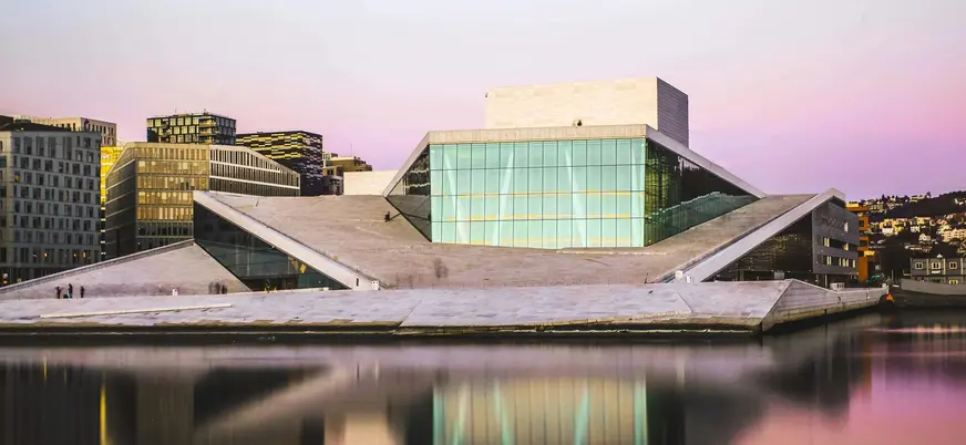 Ópera de Oslo, Noruega, al atardecer, con su arquitectura moderna reflejada en las tranquilas aguas del fiordo.
