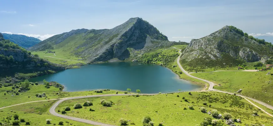 Lago Enol rodeado de praderas y montañas en los Lagos de Covadonga bajo cielo despejado.