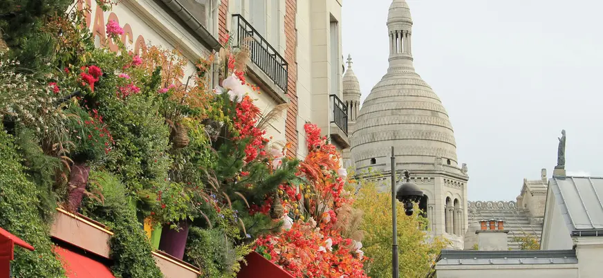 Vista parcial de la Basílica del Sacré-Cœur en Montmartre, París, con una fachada adornada con abundantes flores rojas y verdes en primer plano.