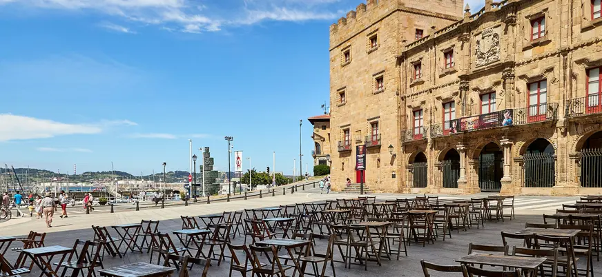 Terraza con mesas frente al Palacio de Revillagigedo y vistas al puerto deportivo de Gijón en un día soleado