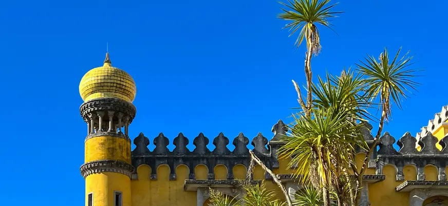 Cúpula amarilla del Palacio da Pena junto a palmeras bajo un cielo azul intenso.