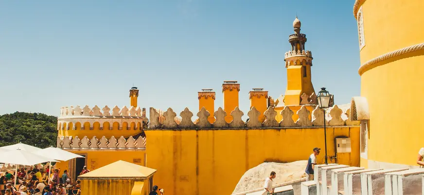 Terraza amarilla del Palacio da Pena con turistas bajo el sol en Sintra.