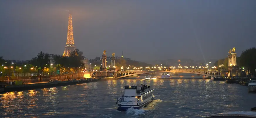Barco navegando el río Sena con la Torre Eiffel iluminada entre la niebla.