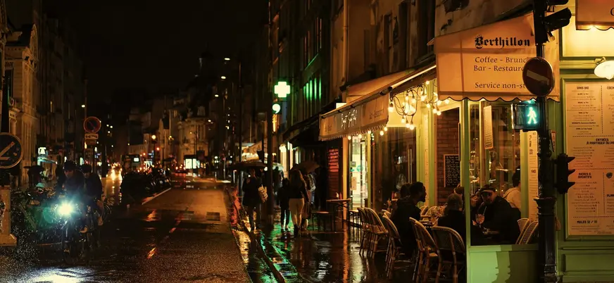 Gente cenando en la terraza iluminada del café Berthillon en una noche de París.