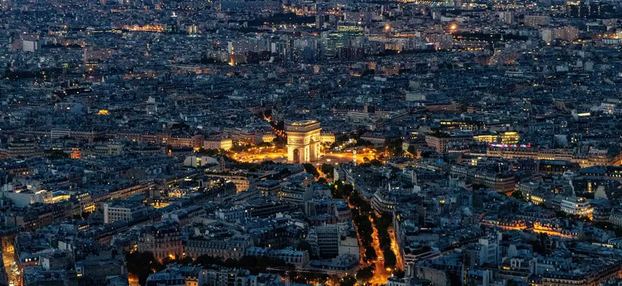 Vista aérea nocturna del Arco del Triunfo iluminado y el horizonte de París.