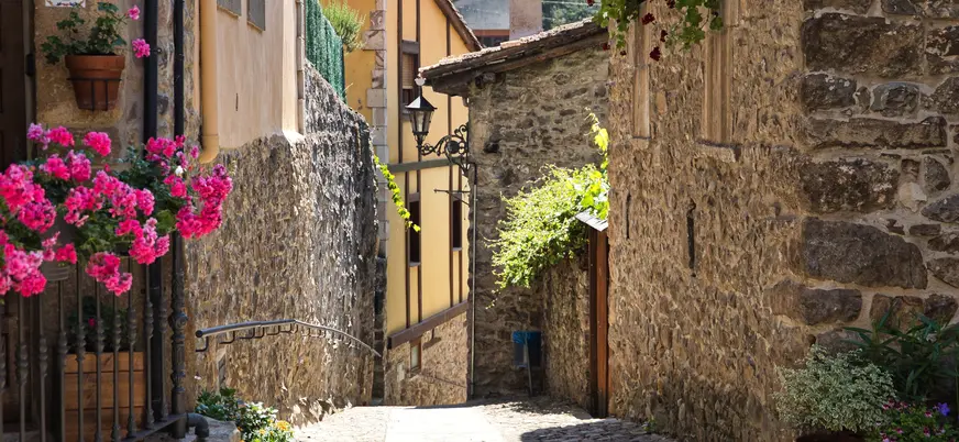 Calle empedrada con casas de piedra y flores en el casco histórico de Potes, Cantabria.