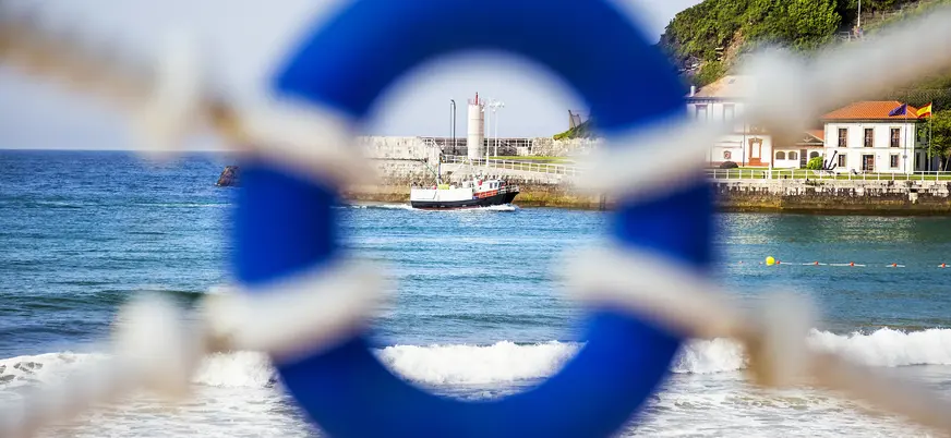 Barco pesquero en el mar enmarcado por un salvavidas azul en Llanes, Asturias.