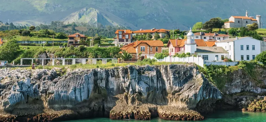 Acantilados de Llanes con casas rurales frente al mar y montañas de Asturias