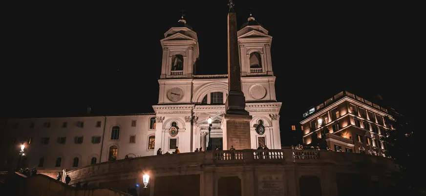 Iglesia Trinità dei Monti iluminada de noche junto al obelisco en Roma