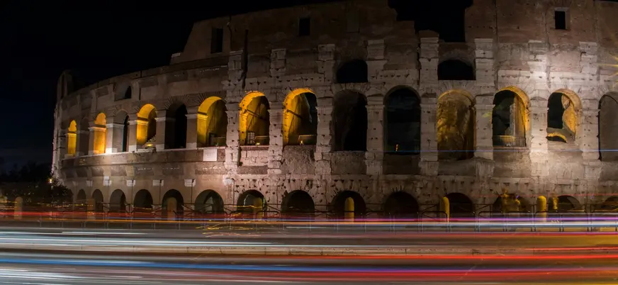 Coliseo de Roma iluminado de noche con estelas de luz de tráfico en la avenida