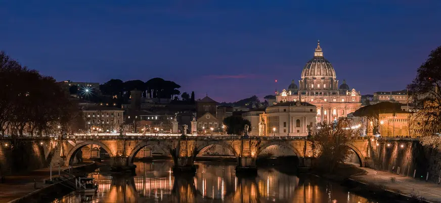 Basílica de San Pedro iluminada al anochecer con el río Tíber y el puente en Roma