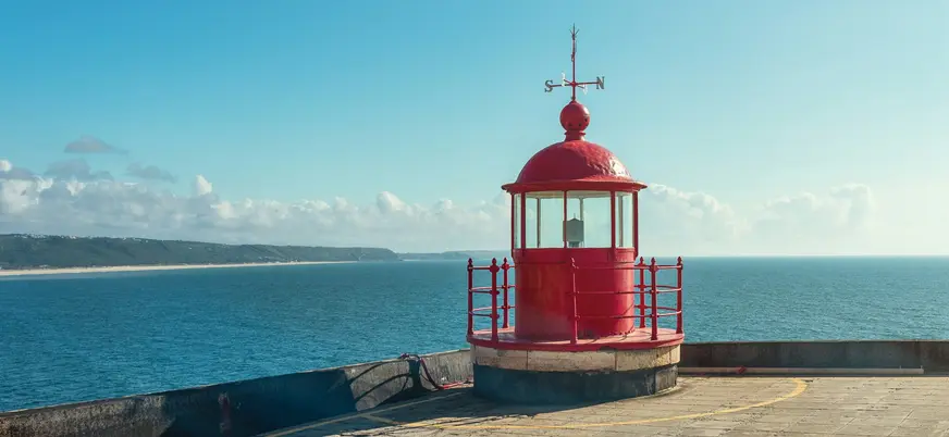 Faro rojo en el fuerte de Nazaré con vistas al océano Atlántico y costa de fondo.