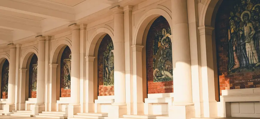 Mosaicos religiosos en la columnata del Santuario de Fátima bajo luz cálida.