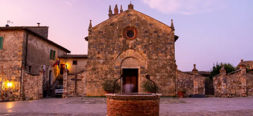 Plaza con iglesia medieval y fuente al atardecer en la Toscana, Italia