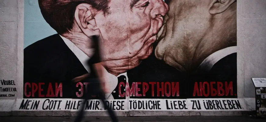 Mural del beso en el Muro de Berlín con silueta de persona caminando delante.