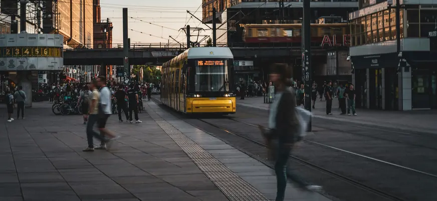 Tranvía amarillo circulando por Alexanderplatz en Berlín con peatones en movimiento.