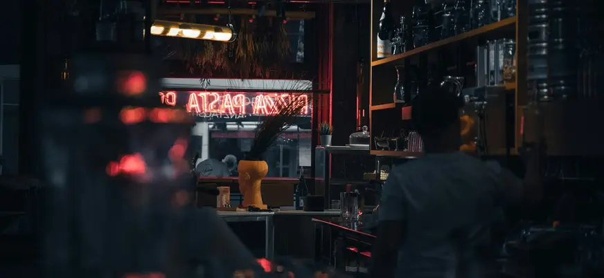 Interior tenue de un bar en Berlín con letrero de neón rojo de pizza y pasta.