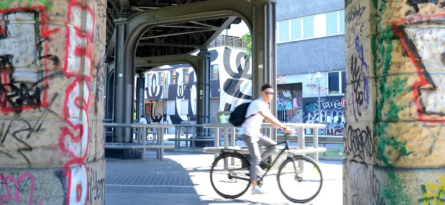 Ciclista pasando bajo una estructura de hierro con grafiti en Berlín.