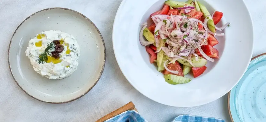 Ensalada griega fresca y salsa tzatziki servidas en platos blancos en Atenas