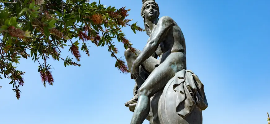 Estatua de guerrero griego con casco y escudo bajo un cielo azul en Atenas