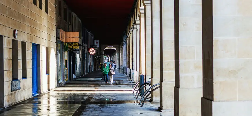 Pareja paseando bajo los soportales de piedra de la Plaza Mayor de Gijón.