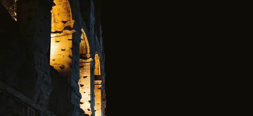 Arcos iluminados del Coliseo Romano resaltando sobre un fondo negro nocturno.