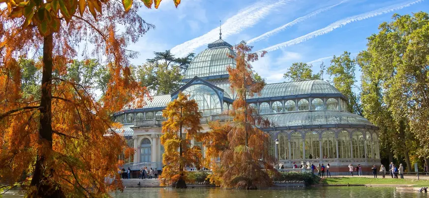 Palacio de Cristal rodeado de árboles y estanque en El Retiro, Madrid.