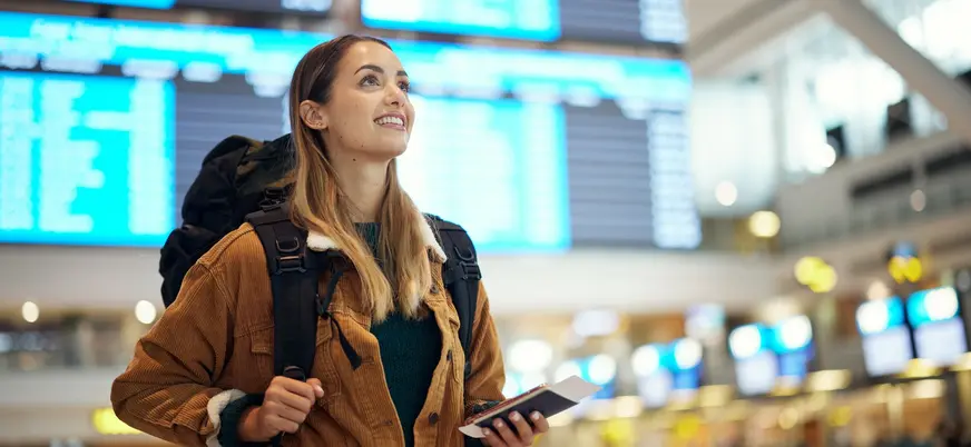 Viajera con mochila y pasaporte en el Aeropuerto de Asturias frente a paneles.