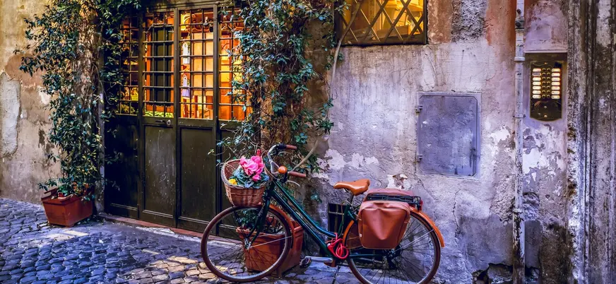 Bicicleta con flores apoyada en una fachada rústica iluminada en una calle de Roma