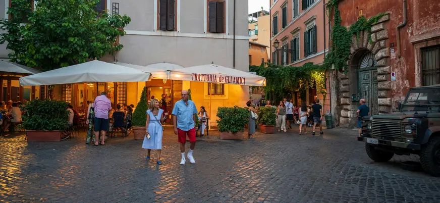 Plaza animada de Trastevere en Roma con una trattoria y gente paseando al atardecer