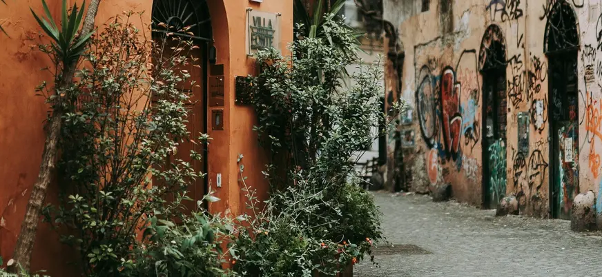 Calle con fachadas envejecidas y plantas en Trastevere, Roma, con muros grafiteados