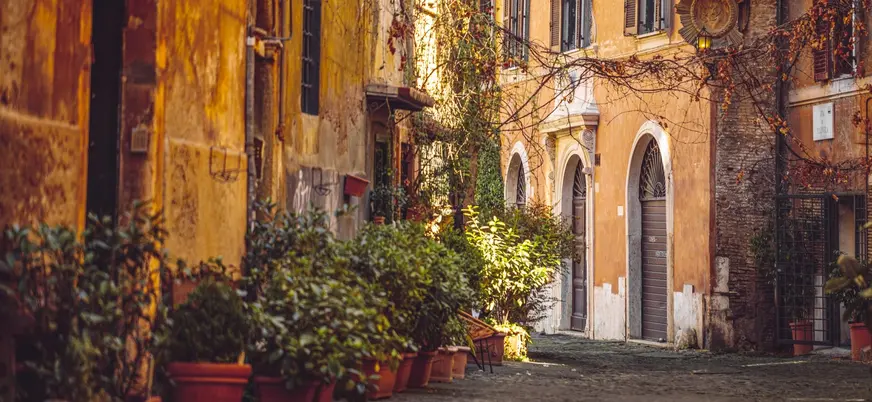Calle tranquila de Trastevere en Roma con fachadas ocres y macetas llenas de plantas