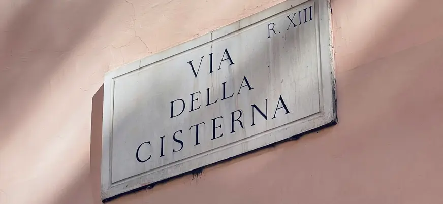 Placa de la Via della Cisterna en una fachada rosada del barrio de Trastevere en Roma