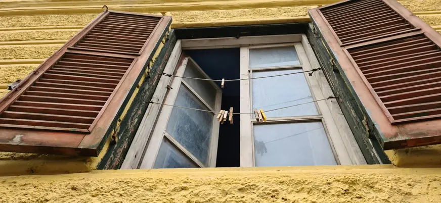 Ventana con contraventanas de madera y pinzas de ropa en una fachada amarilla de Roma