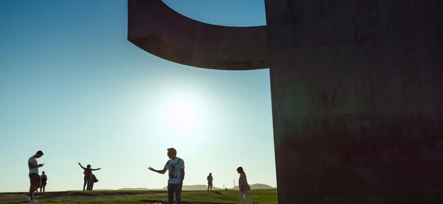 Personas junto al Elogio del Horizonte al atardecer en Gijón